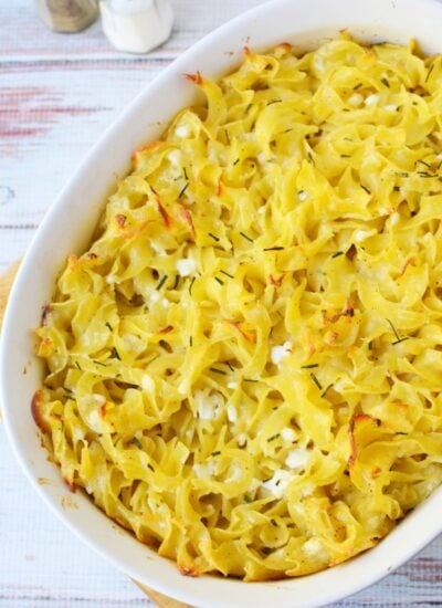 Baked Jackie Kennedy Casserole in a white baking dish with golden egg noodles, browned edges, and fresh chives.