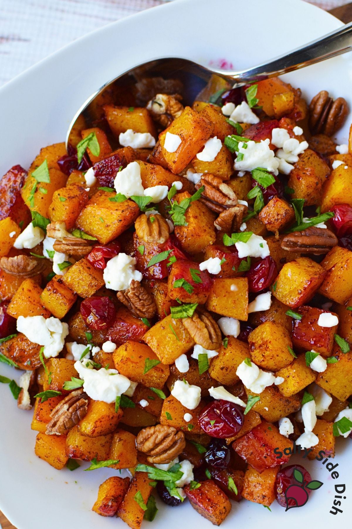 Maple roasted butternut squash with cranberries, crumbled feta, pecan halves, and parsley in a serving bowl.