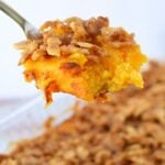 Cooked butternut squash cubes being mashed with a potato masher in a saucepan.