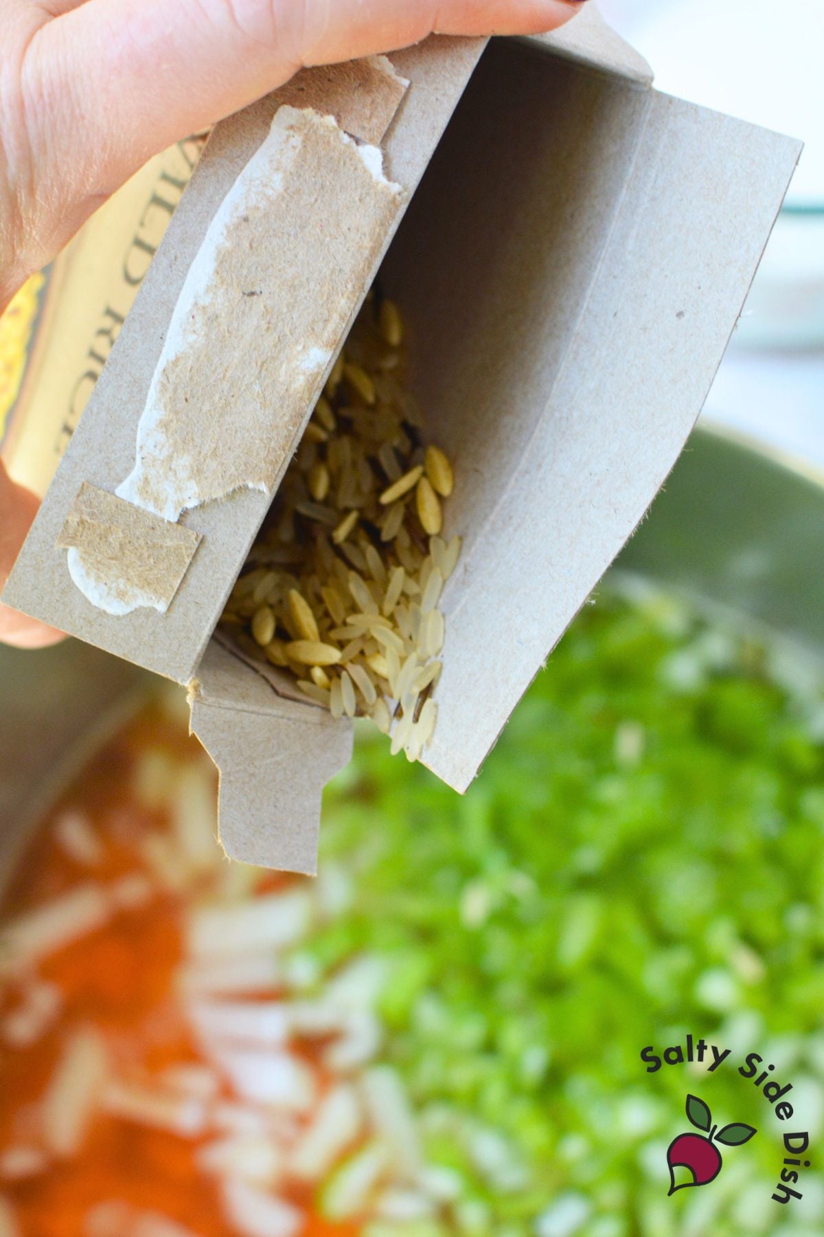 Uncooked long grain and wild rice mix being poured from a box into a pot of chicken wild rice soup