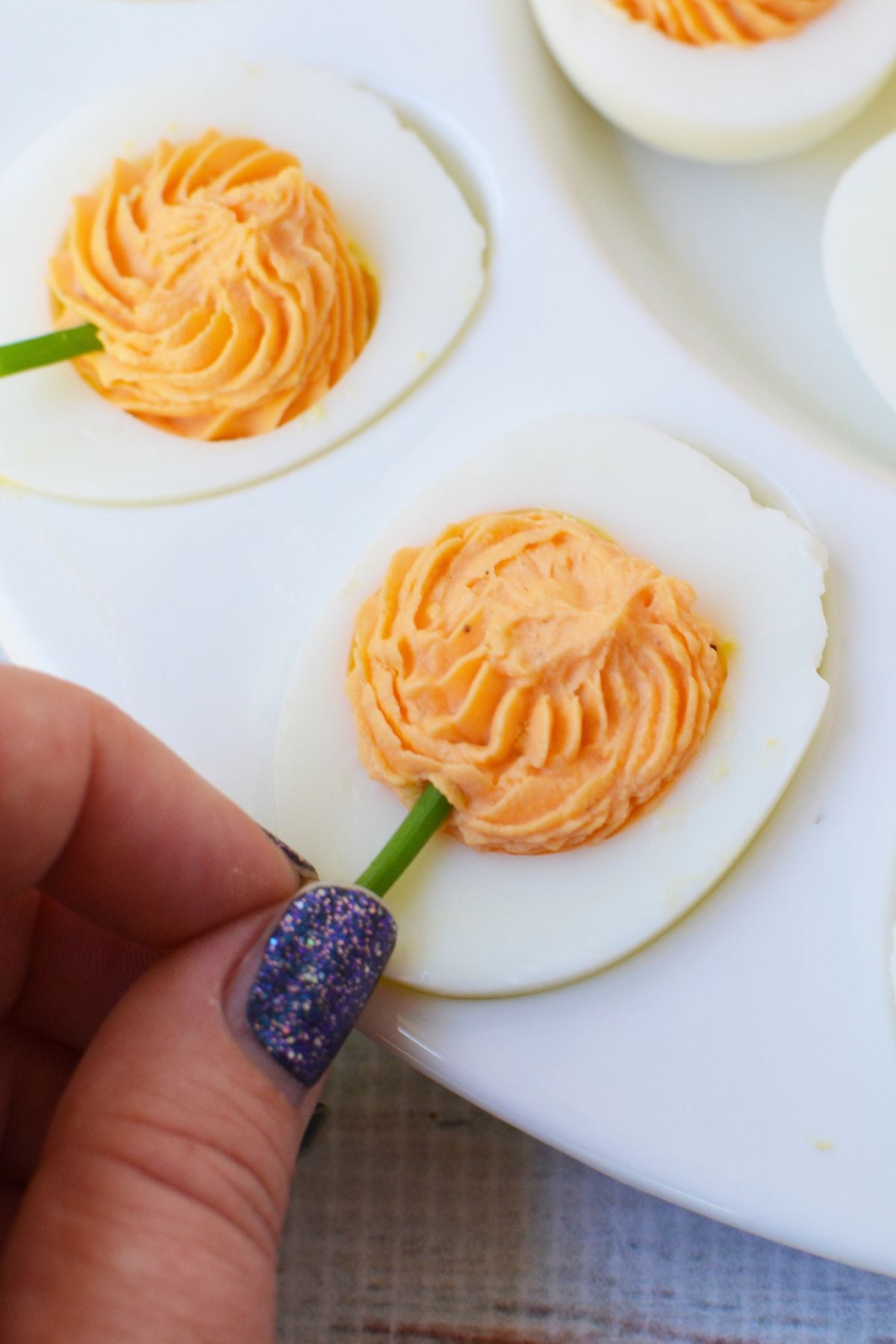 Fresh chive stem being added to orange pumpkin-shaped deviled egg filling for Halloween