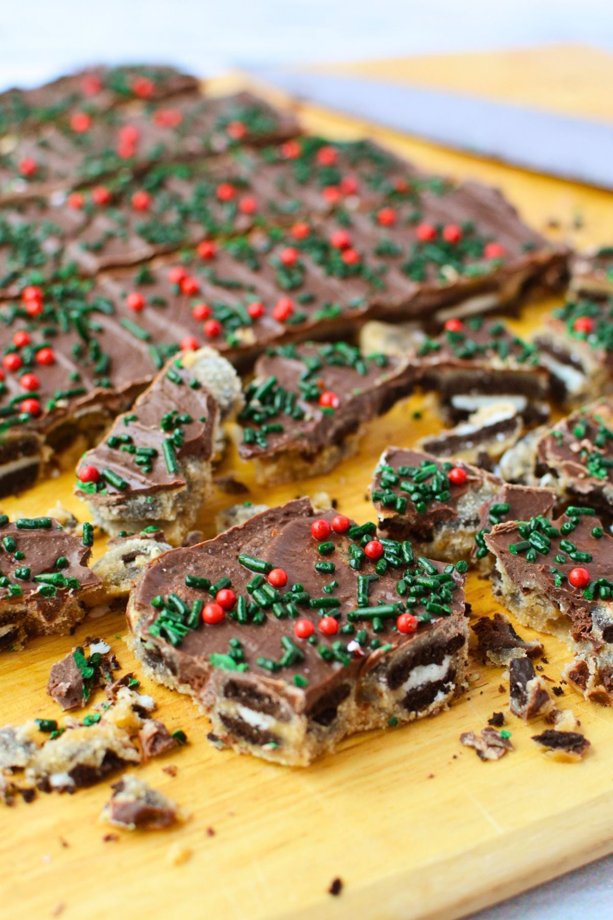Pieces of homemade Oreo Christmas toffee bark topped with green sprinkles and red candy decorations on a wooden board.