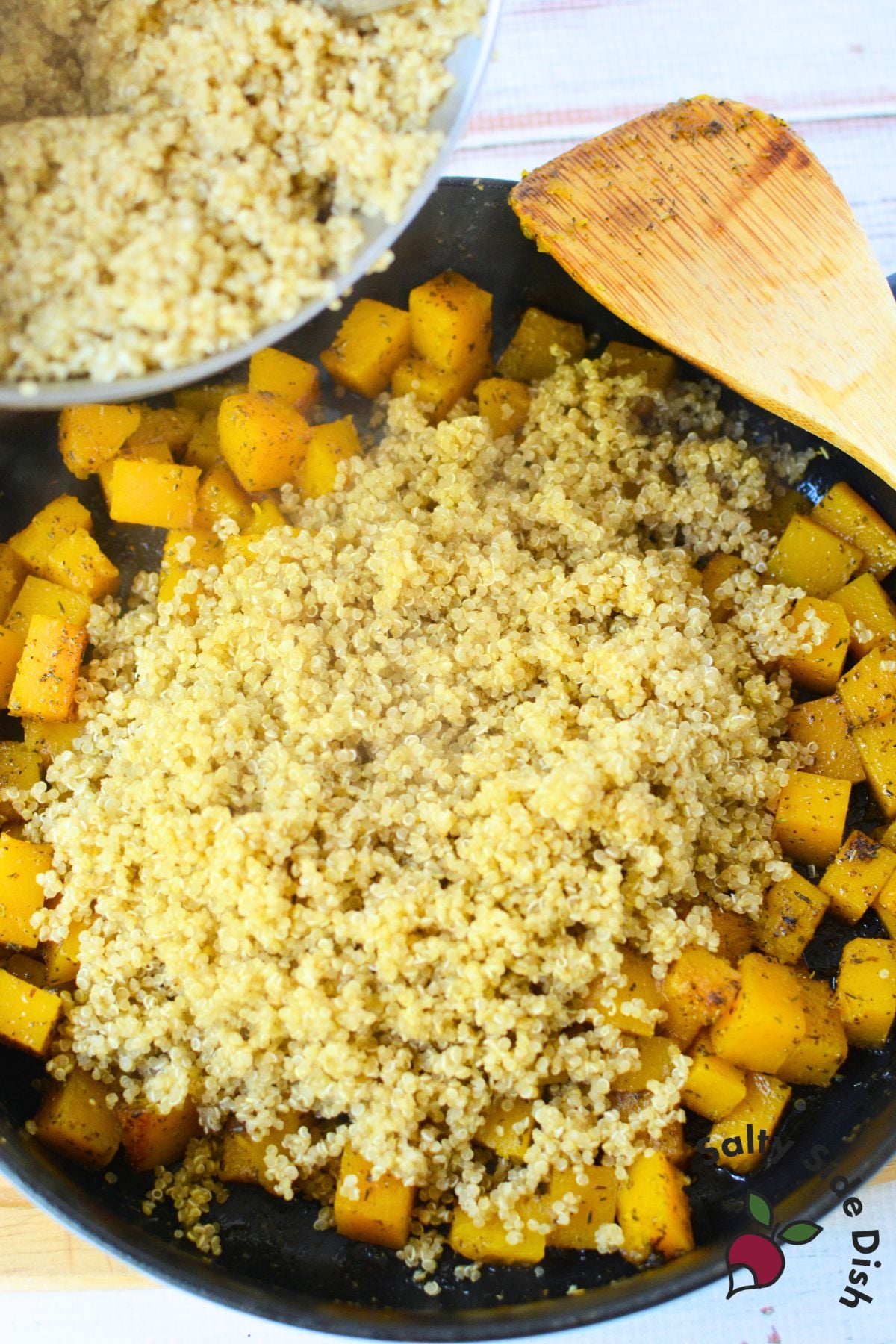 Cooked quinoa being added to a skillet of seasoned butternut squash cubes to make warm quinoa salad.