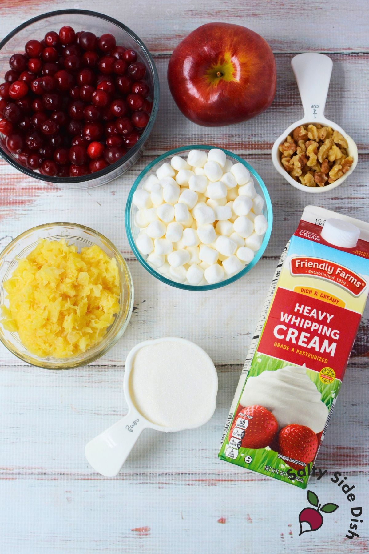 Cranberry salad ingredients including whole cranberries, apple, pineapple, mini marshmallows, sugar, walnuts, and heavy whipping cream.