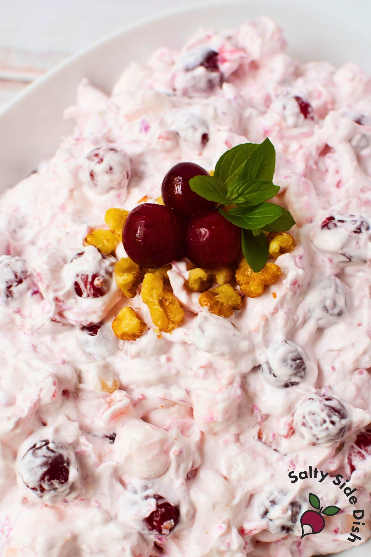 Close-up of creamy cranberry salad topped with whole cranberries, chopped walnuts, and mint.