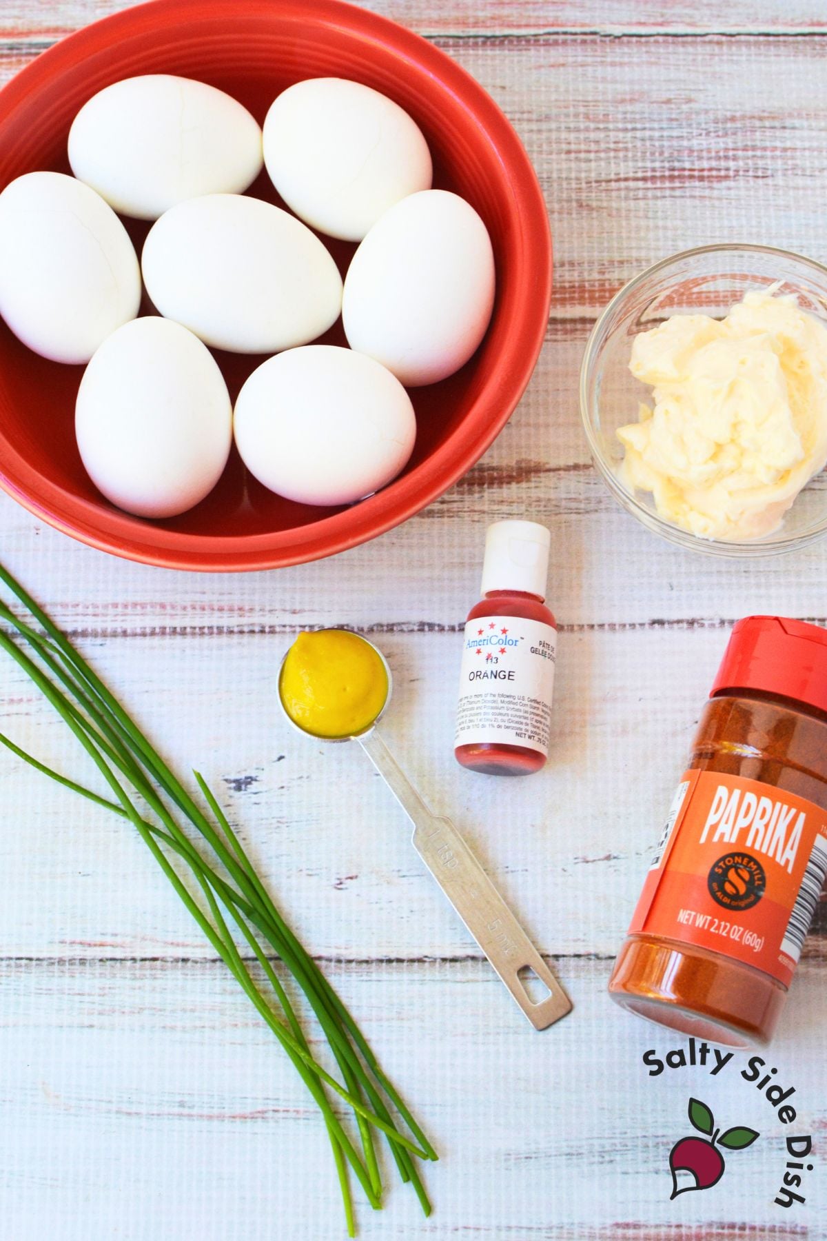Ingredients for Halloween deviled eggs including hard-boiled eggs, mayonnaise, mustard, orange food coloring, chives, and paprika