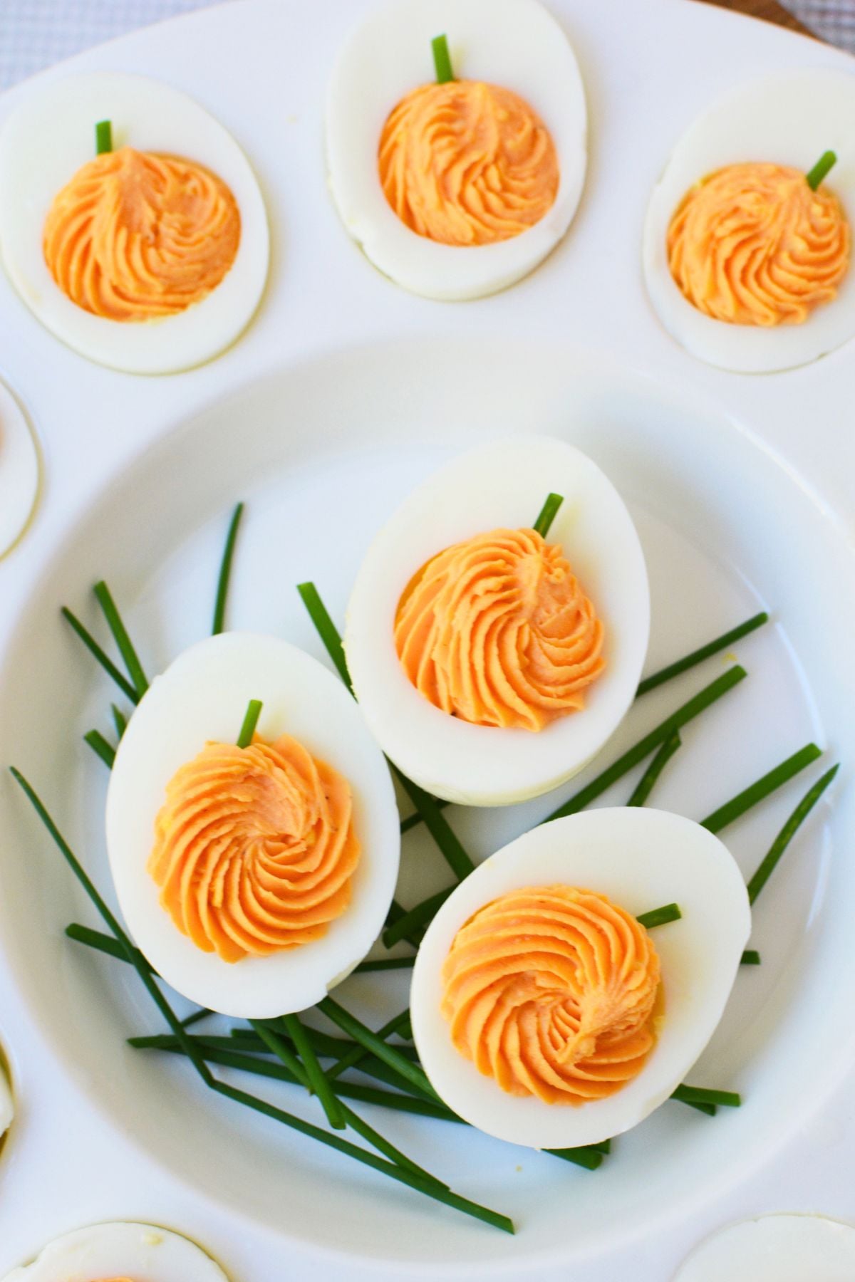 Pumpkin deviled eggs with swirled orange filling and green chive stems on a white serving platter