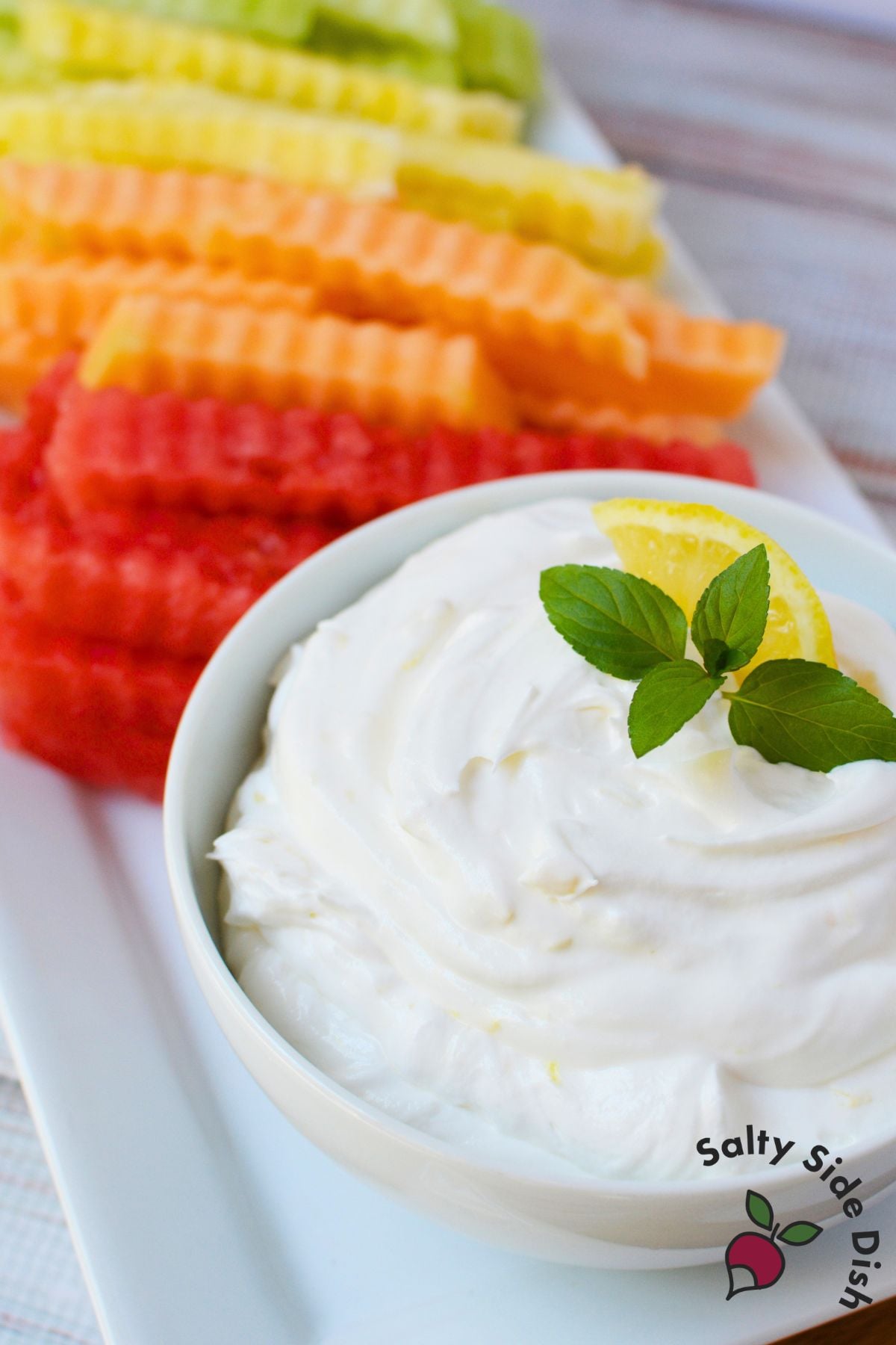 Creamy lemon fruit dip garnished with fresh mint and a lemon wedge, served with colorful crinkle-cut fruit fries.