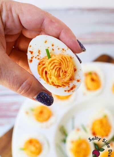 Close-up of Halloween deviled egg with orange pumpkin-shaped filling, chive stem, and paprika