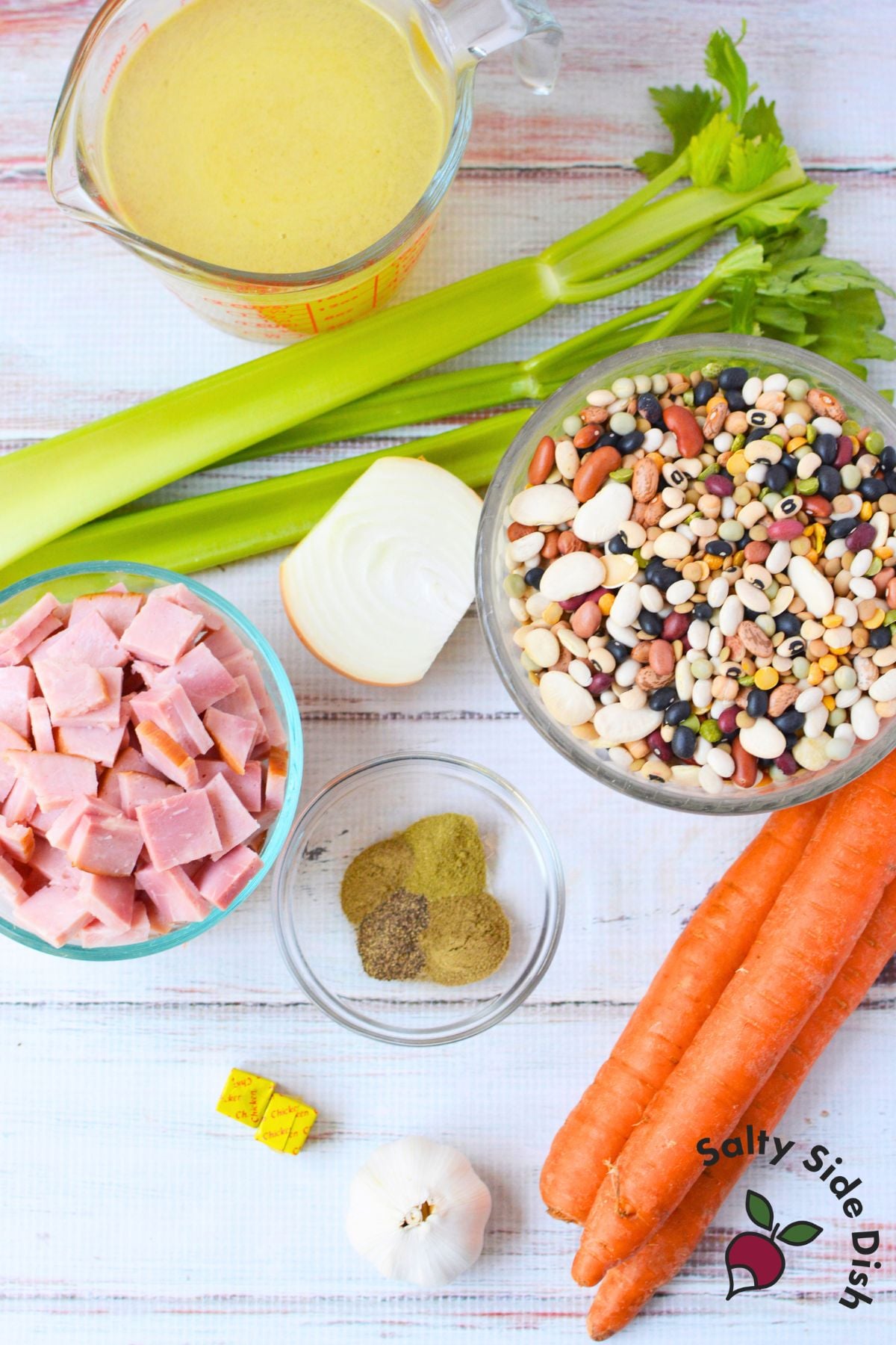 Ingredients for ham and bean soup including dried 16-bean mix, chopped ham, carrots, celery, onion, garlic, chicken broth, and seasoning