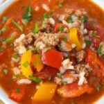 Close-up of stuffed pepper soup with ground beef, red and orange bell peppers, white rice, and tomatoes in a savory broth.