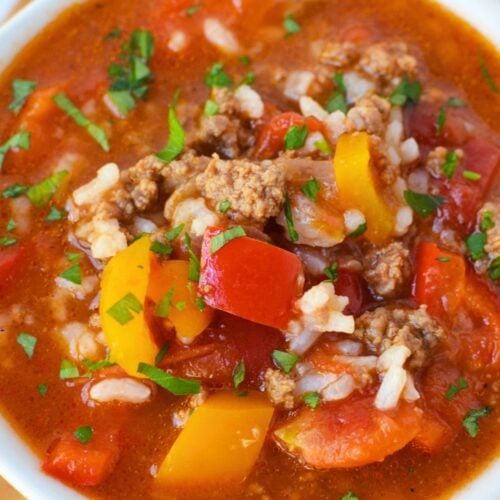 Close-up of stuffed pepper soup with ground beef, red and orange bell peppers, white rice, and tomatoes in a savory broth.