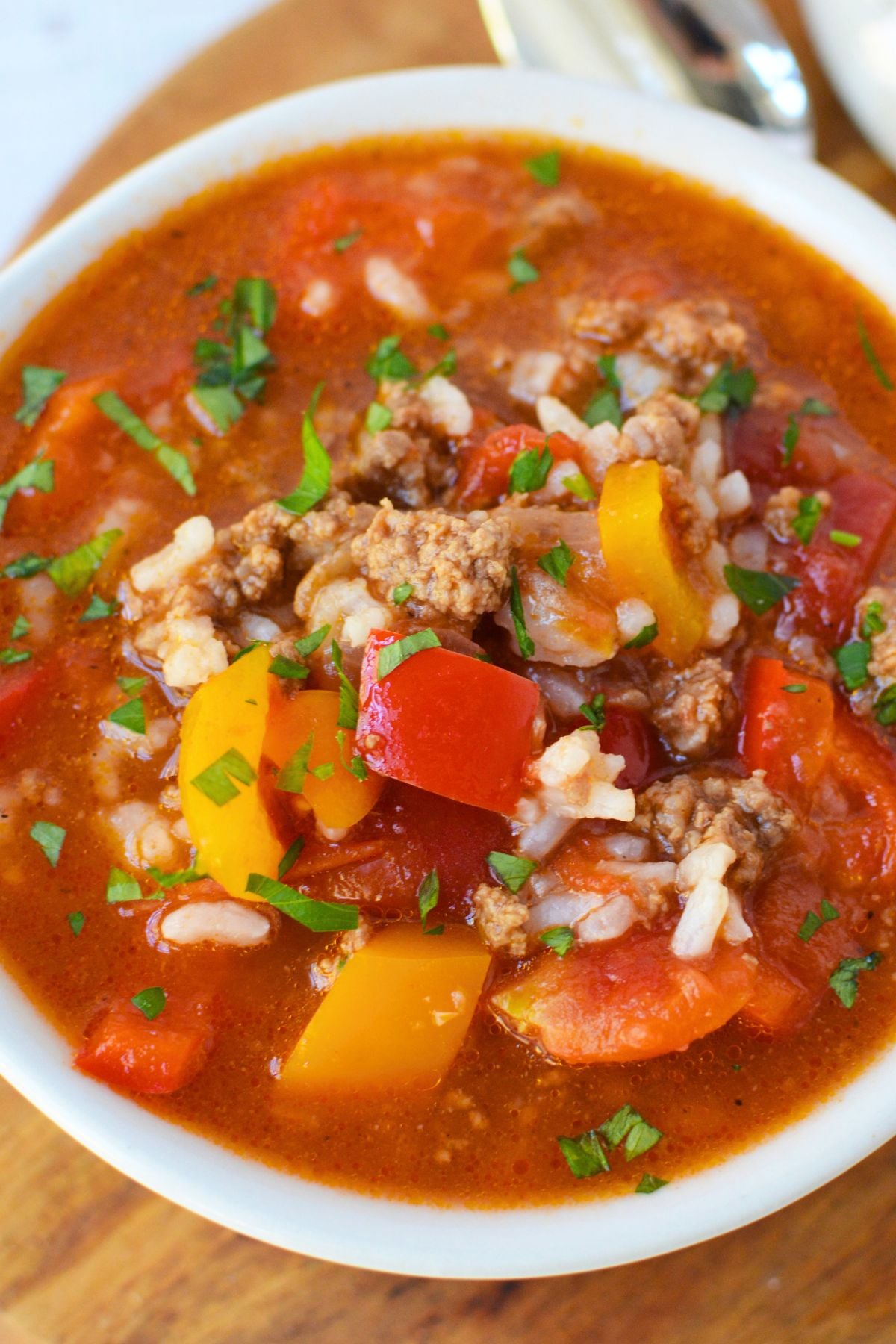 Close-up of stuffed pepper soup with ground beef, red and orange bell peppers, white rice, and tomatoes in a savory broth.