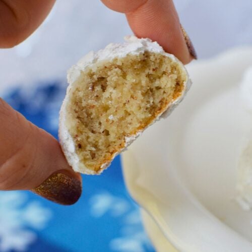 Homemade almond snowball cookie broken in half to show its buttery, crumbly interior beneath a powdered sugar coating.