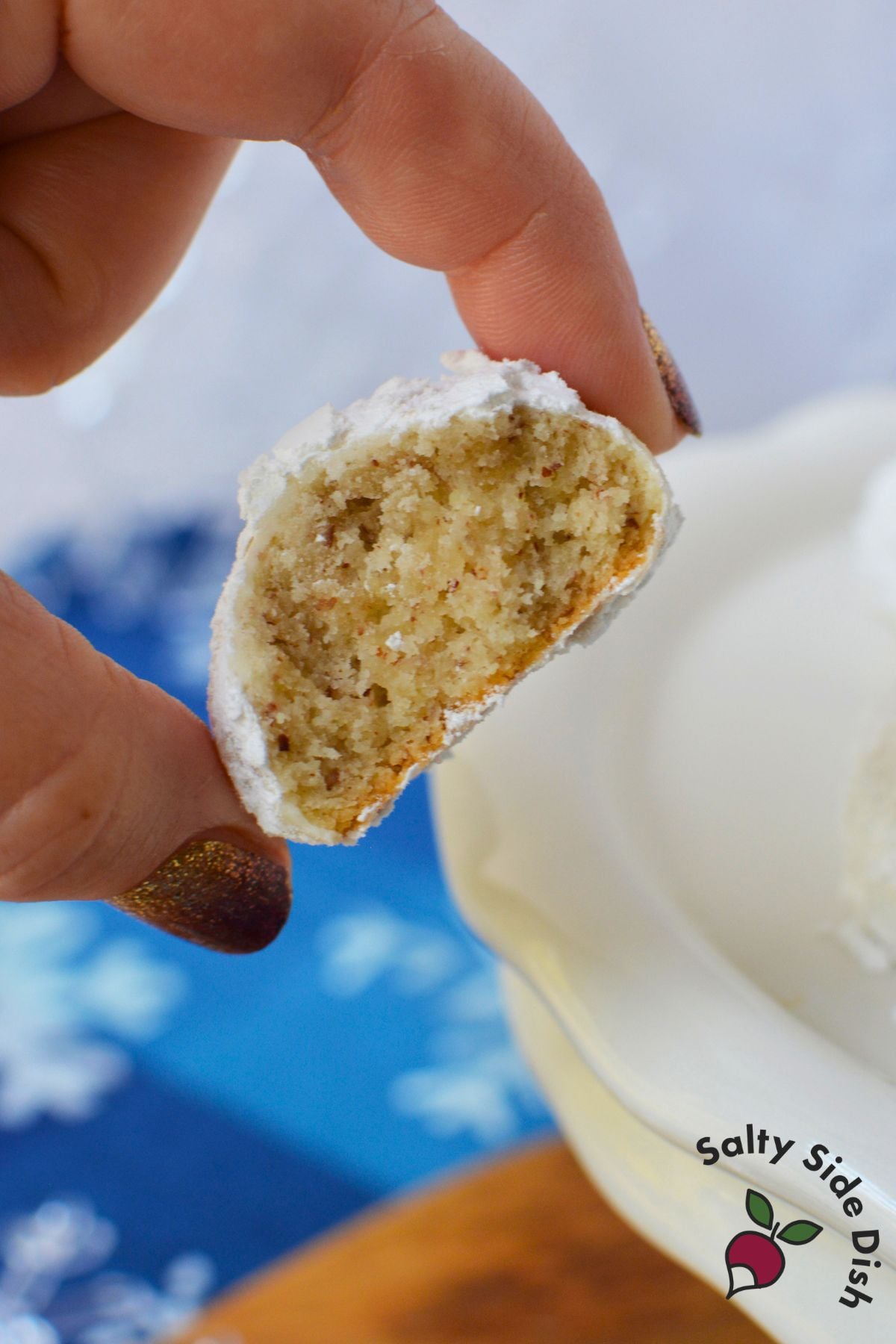Homemade almond snowball cookie broken in half to show its buttery, crumbly interior beneath a powdered sugar coating.