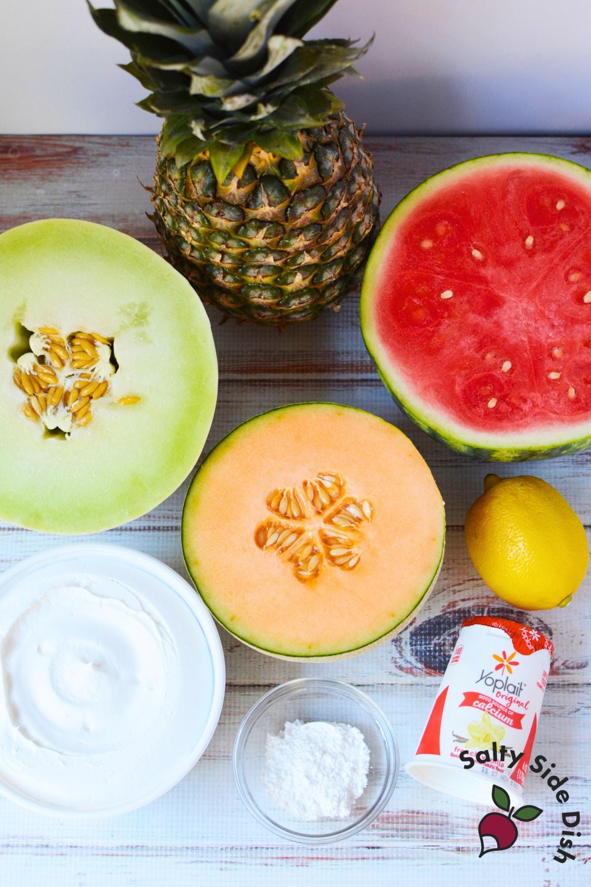 Ingredients for homemade fruit fries with lemon dip, including watermelon, pineapple, cantaloupe, honeydew, yogurt, lemon, Cool Whip, and powdered sugar