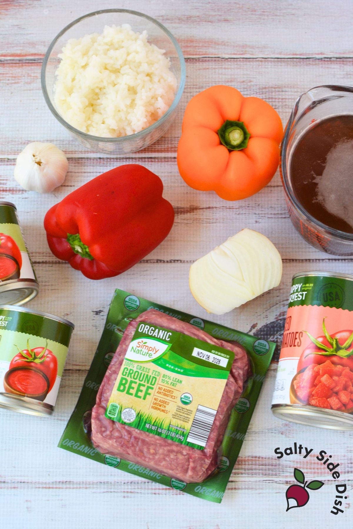Ingredients for stuffed pepper soup including ground beef, red and orange bell peppers, cooked white rice, beef broth, tomato sauce, diced tomatoes, onion, and garlic.