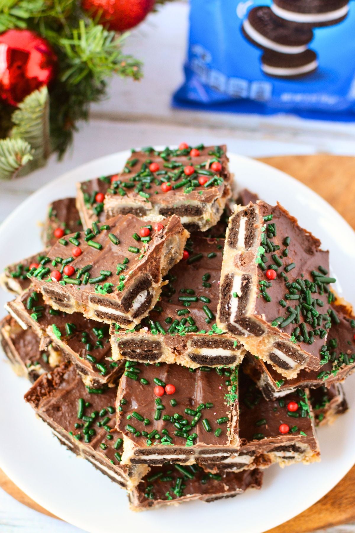 Stacked pieces of Oreo toffee bark showing whole Mini Oreo cookies beneath chocolate and brown sugar toffee, decorated with red and green sprinkles.
