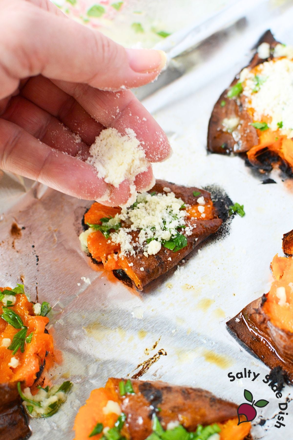 Hand sprinkling grated Parmesan over smashed sweet potato rounds topped with garlic butter and parsley.