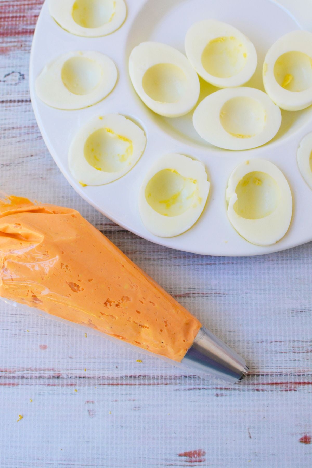 Orange deviled egg filling in a piping bag next to halved hard-boiled egg whites ready to fill