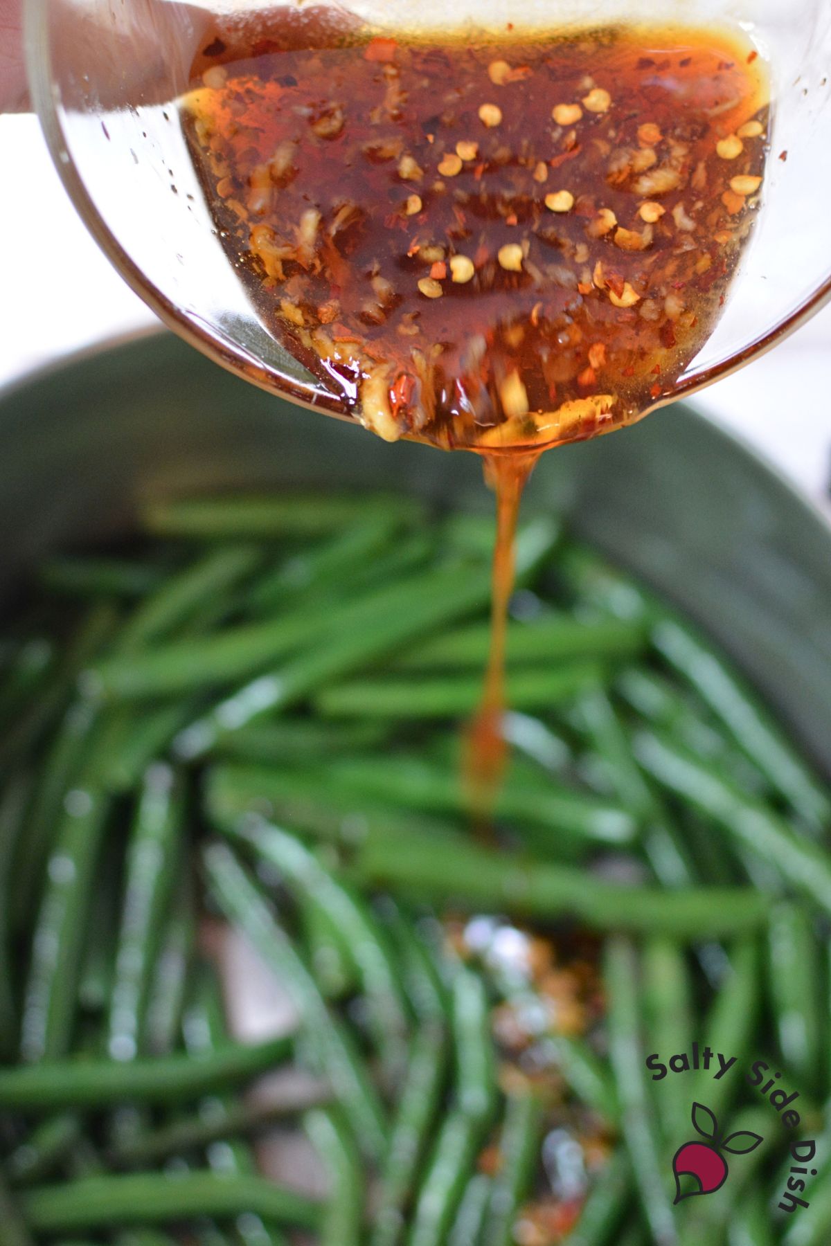 Honey garlic sauce being poured over green beans in a pot.
