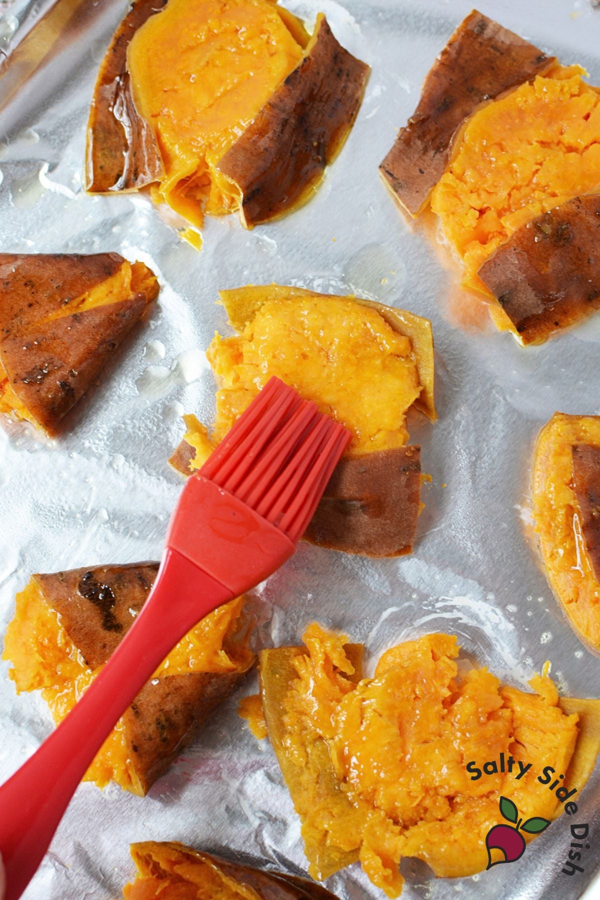 Olive oil being brushed over smashed sweet potato rounds before roasting.
