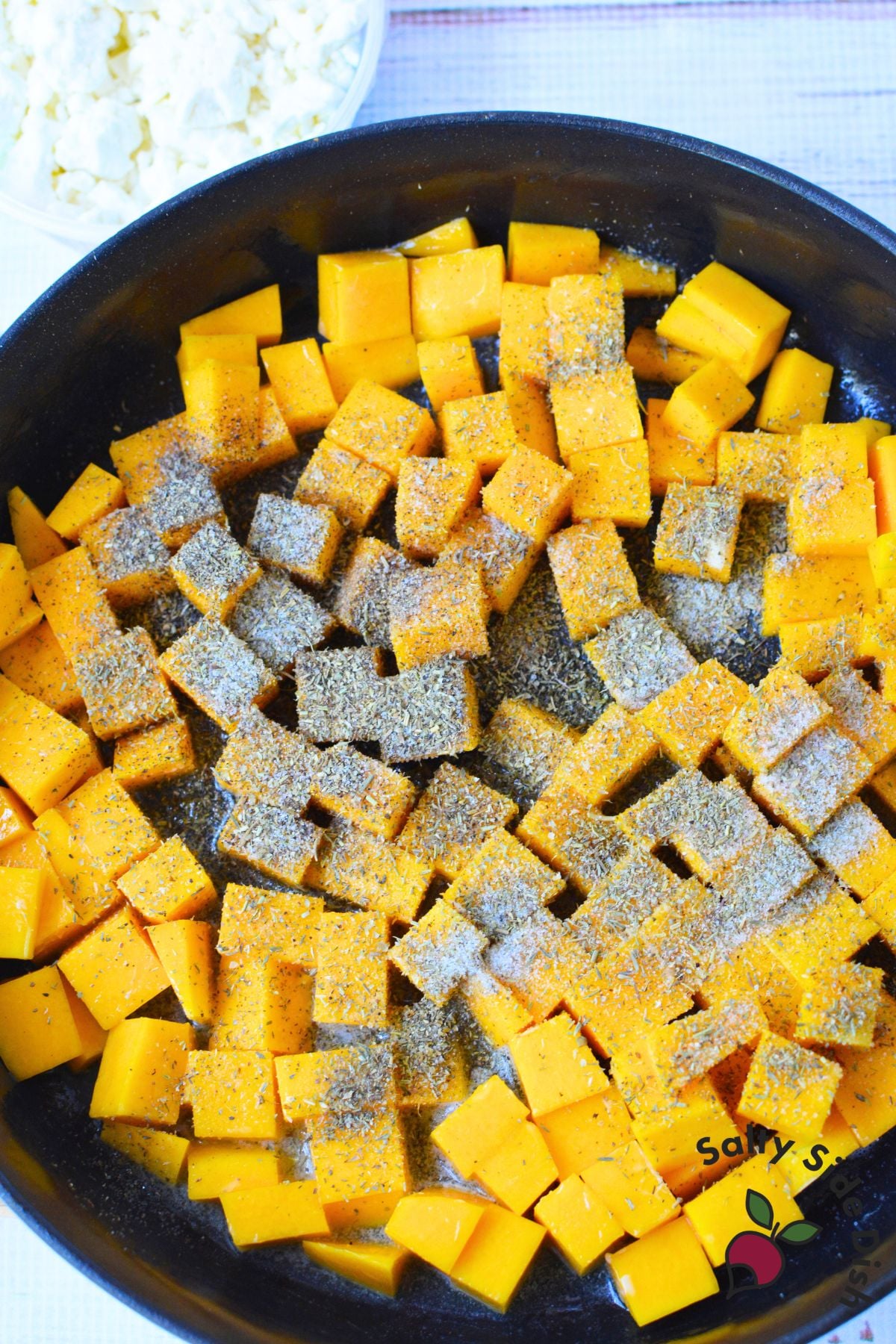 Cubed butternut squash sprinkled with Italian seasoning, salt, and pepper in a skillet with melted butter.