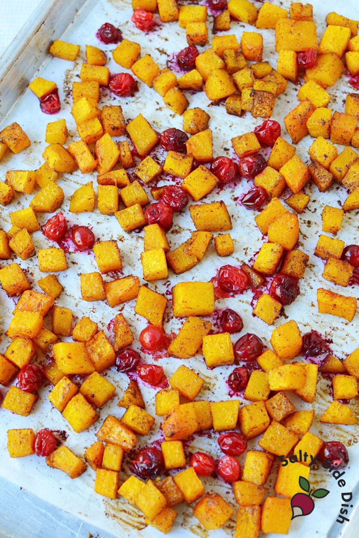 Roasted butternut squash cubes with browned edges and softened cranberries on a parchment-lined baking sheet.