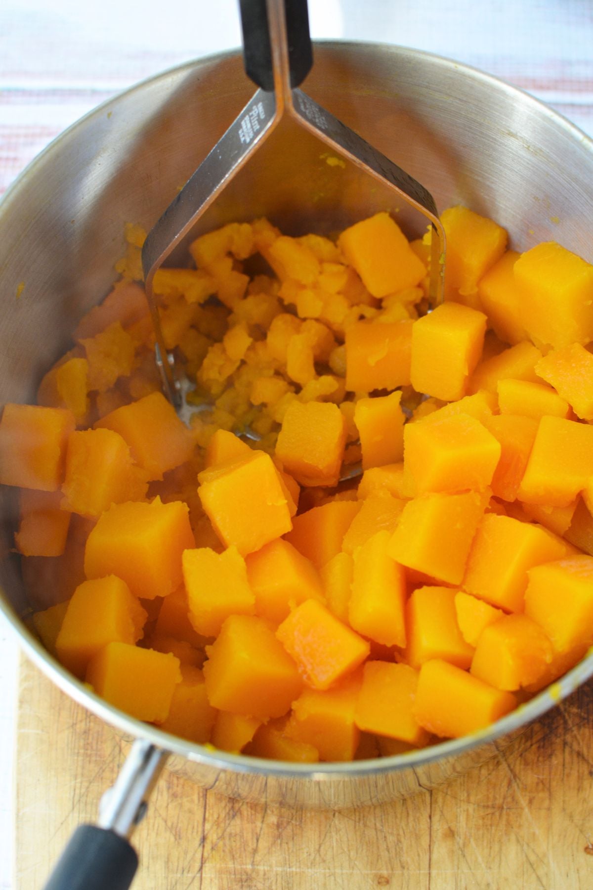 Mashed butternut squash combined with milk and whole eggs in a saucepan before mixing the casserole filling.