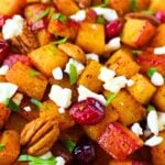 Close-up of roasted butternut squash topped with cranberries, feta, pecans, and chopped parsley.