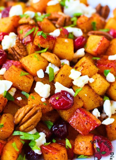 Close-up of roasted butternut squash topped with cranberries, feta, pecans, and chopped parsley.