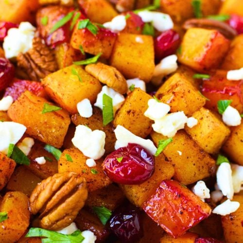 Close-up of roasted butternut squash topped with cranberries, feta, pecans, and chopped parsley.