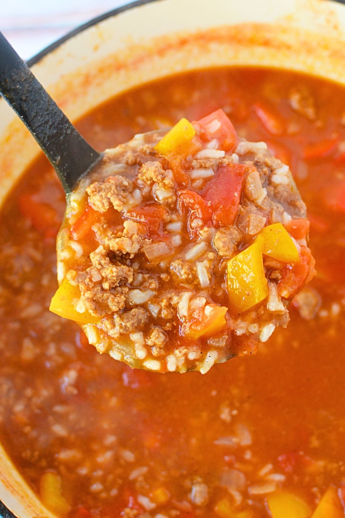 Ladle filled with ground beef, cooked white rice, tomatoes, and bell peppers above a pot of stuffed pepper soup.
