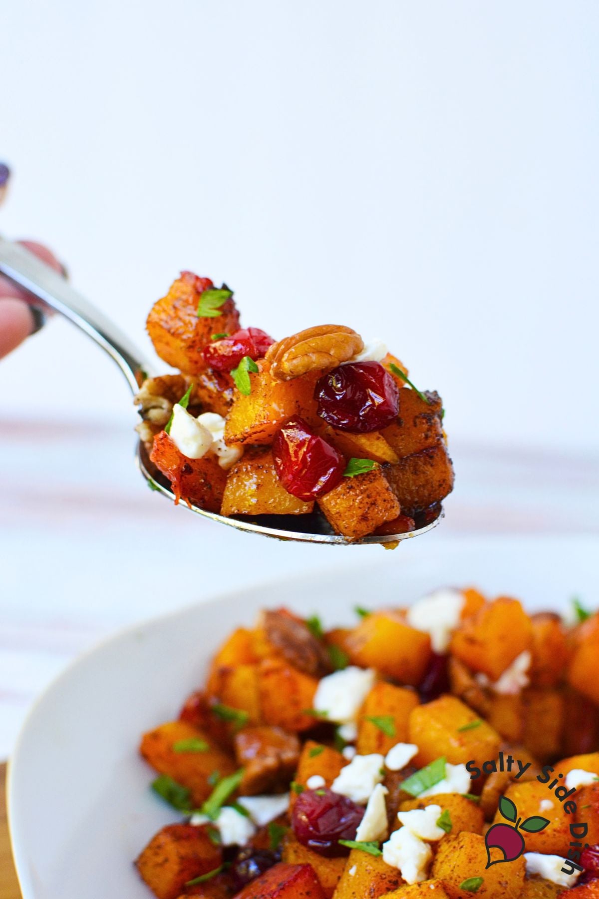 Spoonful of roasted butternut squash with cranberries, feta, and pecans lifted above the serving bowl.