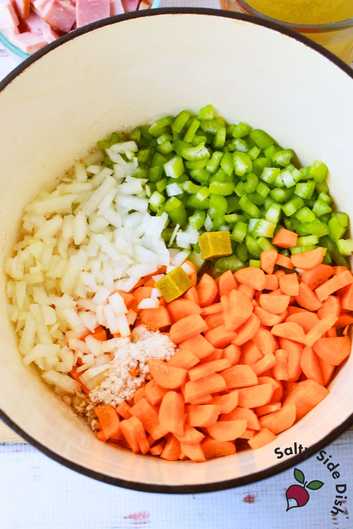 Chopped carrots, celery, and onion with chicken bouillon cubes in a Dutch oven for ham and bean soup.