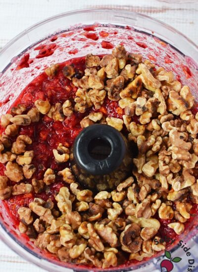 Toasted walnuts added to chopped cranberry orange mixture in a food processor