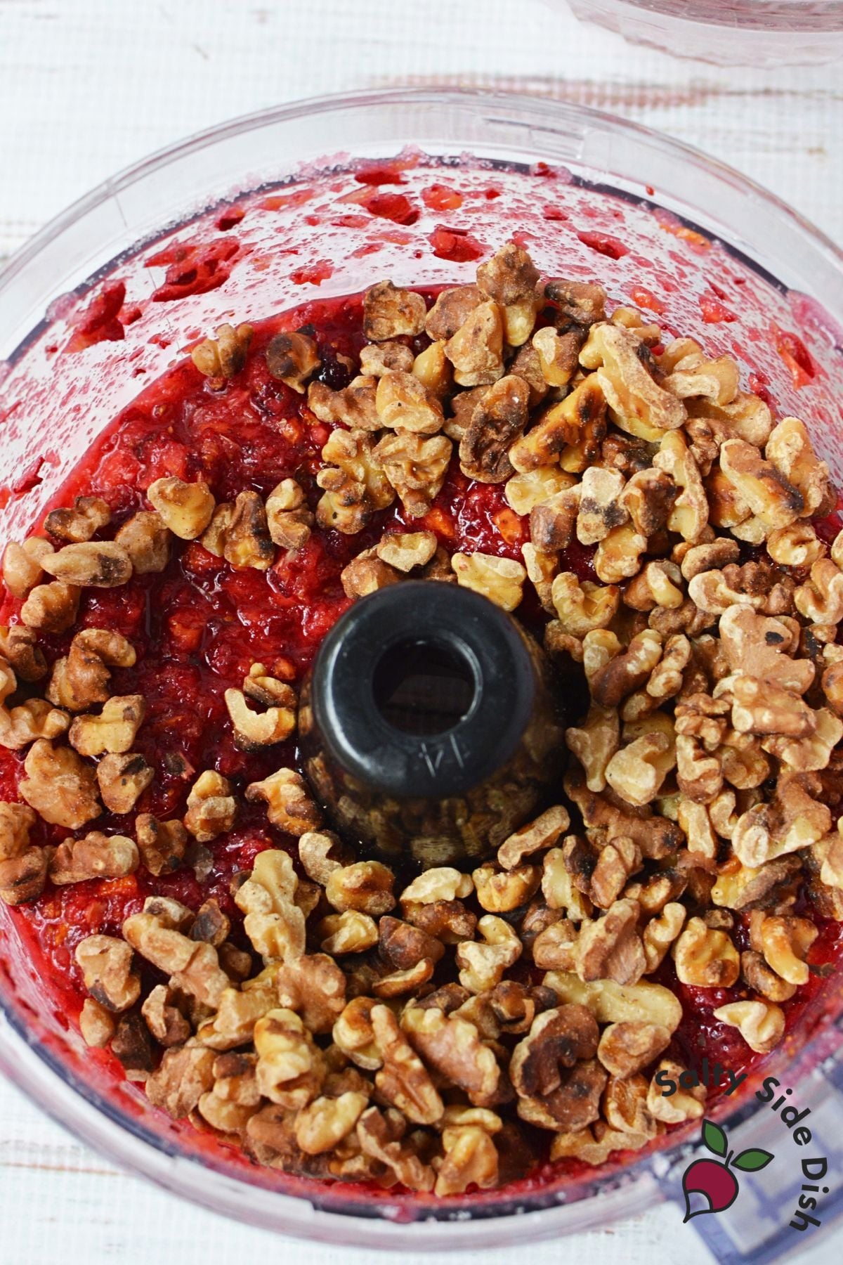 Toasted walnuts added to chopped cranberry orange mixture in a food processor