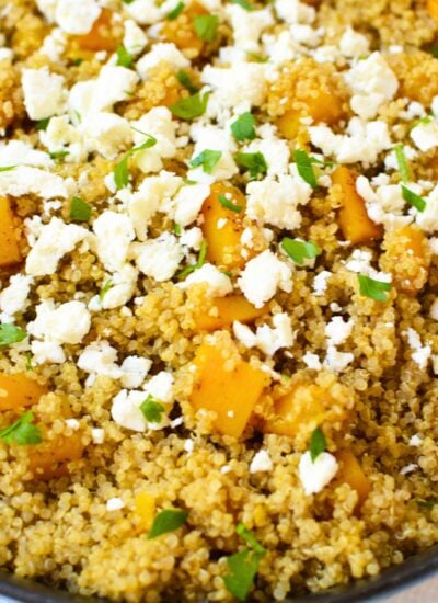 Close-up of warm quinoa and butternut squash salad topped with crumbled feta cheese and chopped fresh parsley.